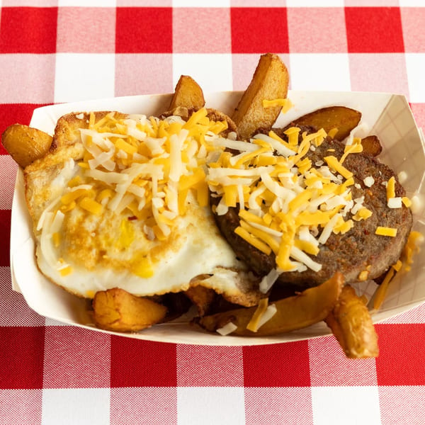 Breakfast platter with fried eggs, sausage patty, and potato wedges, all topped with shredded cheese.