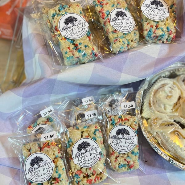 Packaged Rice Krispie treats with red and blue sprinkles, alongside a tray of cinnamon rolls.