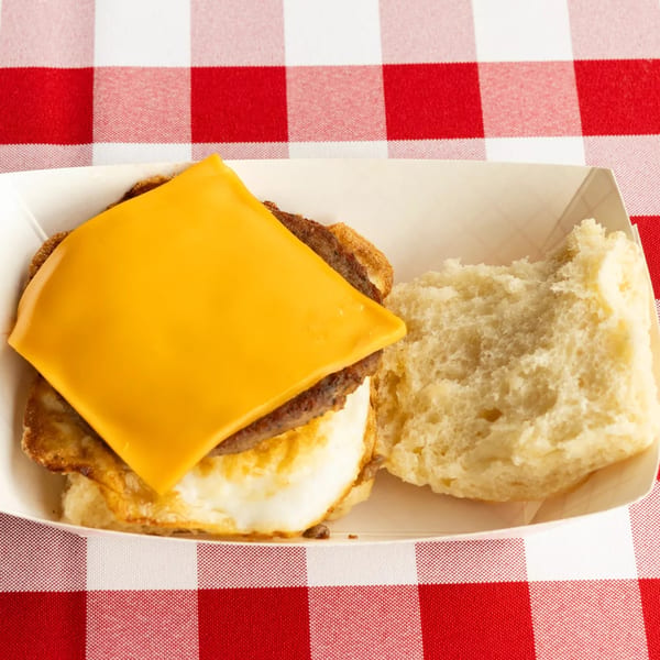 A breakfast sandwich with sausage, egg, and cheese on a biscuit, served in a paper tray.