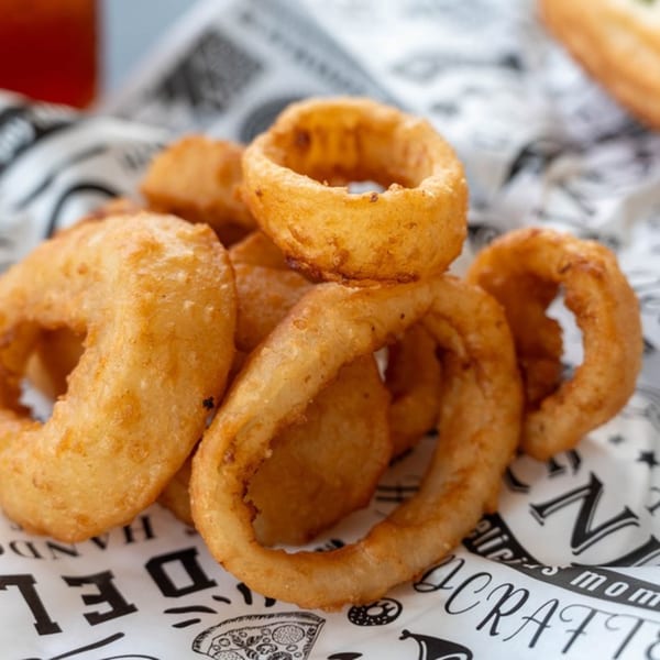 Golden-brown onion rings piled on white paper with black text, ready to be served.