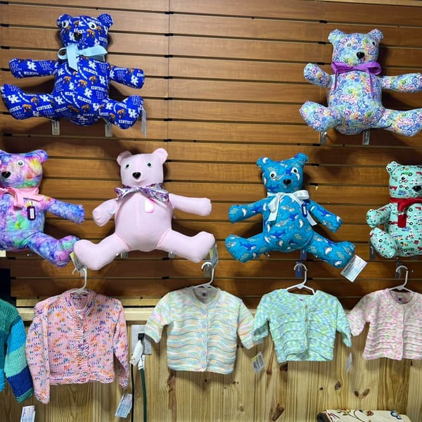 Colorful teddy bears and knitted baby sweaters displayed on a wooden slat wall.