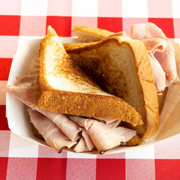 A turkey sandwich on toasted bread in a paper tray, on a red and white checkered tablecloth.